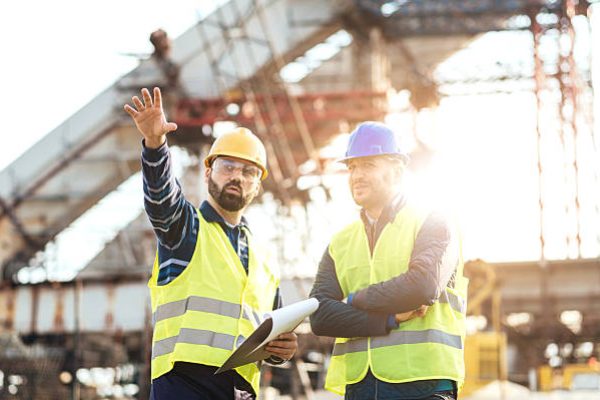 Two experts engineers in protective helmets and fluorescent vests showing the construction site and building activities after the successful project phase. Image taken with Nikon D800 and 85mm developed from RAW in XXXL size, in Novi Sad, Serbia, Central Europe, Europe